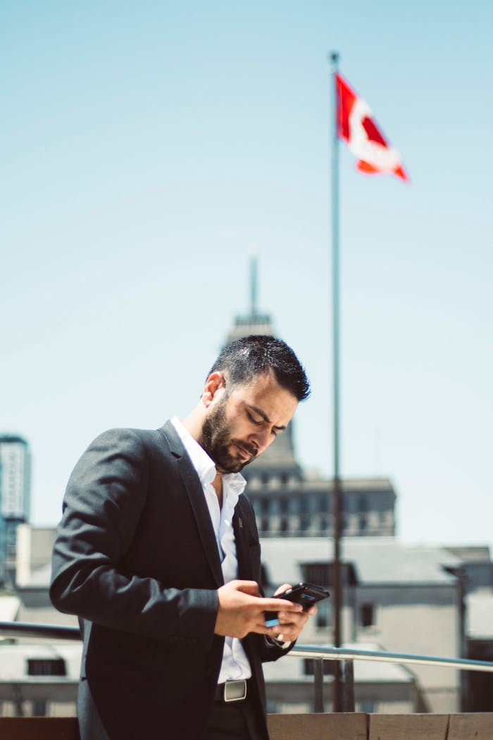 Businessman standing outdoors, using phone with Canadian flag in the background.